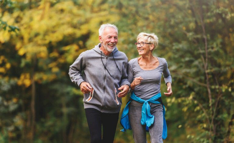 Pasangan yang lebih tua jogging di taman dan tersenyum