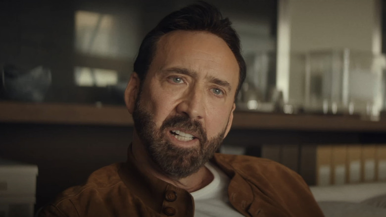 Nick Cage dari Nicolas Cage melihat ke seberang bingkai sambil duduk di dalam The Unbearable Weight of Massive Talent