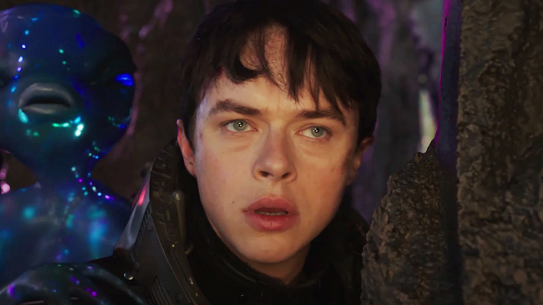 Valerian Dane DeHaan tampak khawatir berdiri di depan alien di Valerian dan Kota Seribu Planet