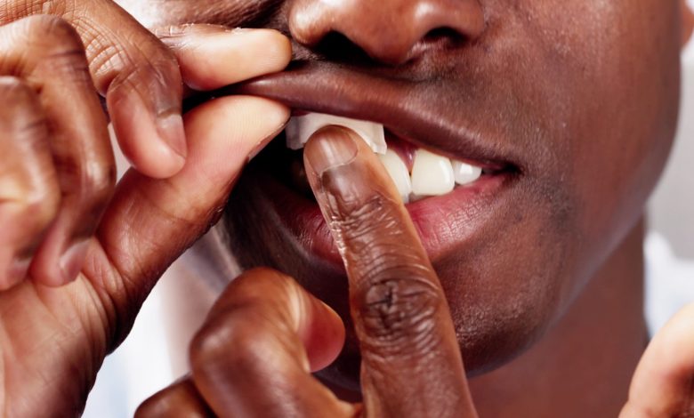 Gambar close-up seorang pria membuka mulutnya sambil memasukkan kantong nikotin di antara bibir dan gusinya.
