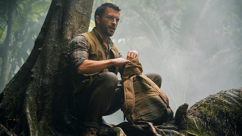 Jonathan Bailey sebagai Dr. Henry Loomis berjongkok di hutan di Jurassic World Rebirth