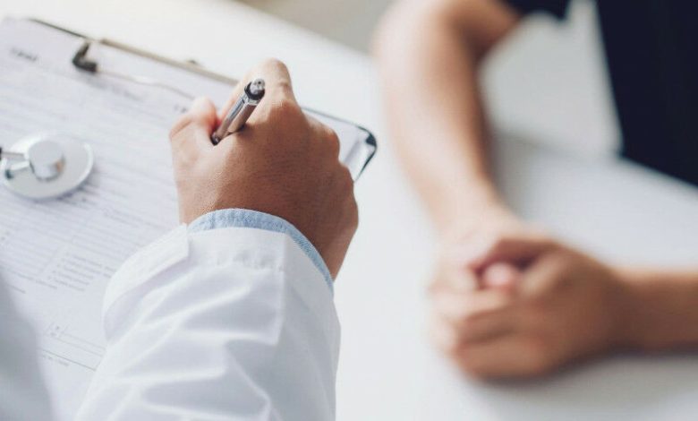 Tangan seorang dokter di mantel lab putih menulis catatan selama konsultasi