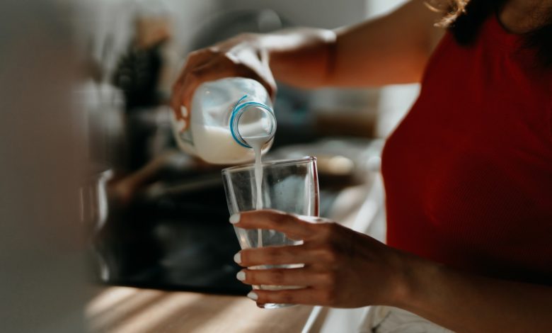 Close-up seseorang menuangkan susu dari botol plastik ke gelas di dapur.