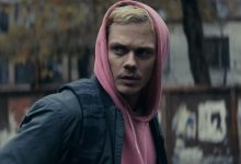 Eddie Bill Skarsgard dalam hoodie merah muda berdiri di jalanan