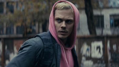 Eddie Bill Skarsgard dalam hoodie merah muda berdiri di jalanan