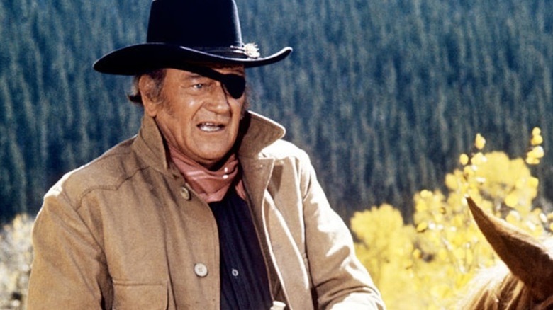John Wayne naik tinggi di sadel sebagai ayam jantan Cogburn dalam grit sejati