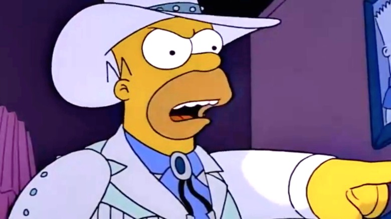 Homer Simpson mengenakan pakaian koboi putih dengan topi yang serasi, menunjuk ke Marge Simpson yang tak terlihat