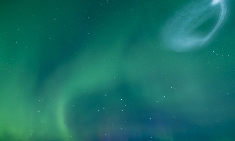 Paduan gas yang terang terlihat di langit malam terhadap aurora hijau bersinar