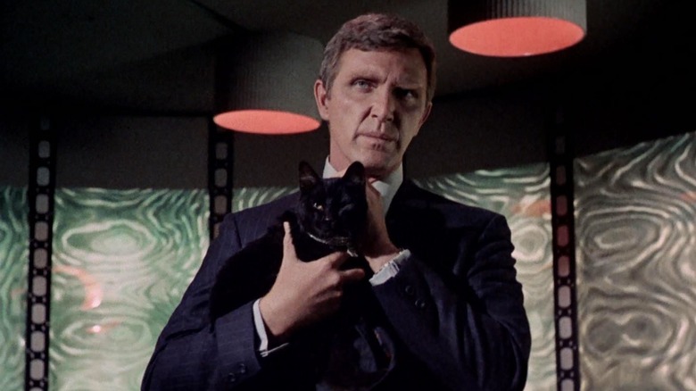 Gary Seven berdiri di atas bantalan transporter, memegang kucing hitam. Adegan dari Star Trek.