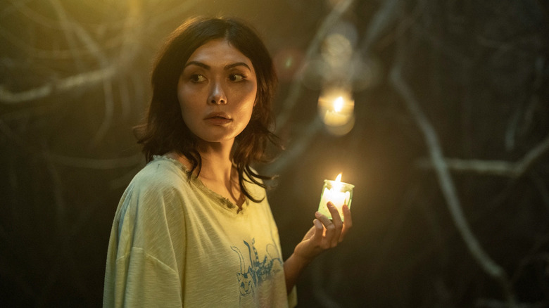 Idalia memegang lilin di malam hari di bawah pohon di Tales of the Walking Dead