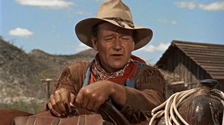 John Wayne bersandar pada pelana kuda sebagai Hondo Lane di Hondo