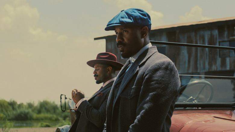 Michael B Jordan sebagai asap dan tumpukan bersandar pada mobil mereka di Sinners