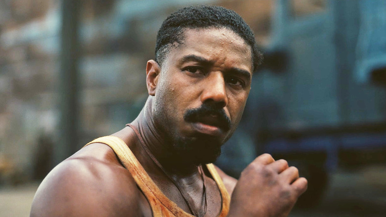 Michael B Jordan sebagai Elijah 'Smoke' Moore, duduk di tanah di luar penggergajian, di Sinners