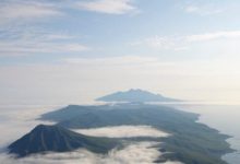 Foto tiga gunung berapi yang membentang ke arah cakrawala, diambil dari puncak salah satu puncak lainnya