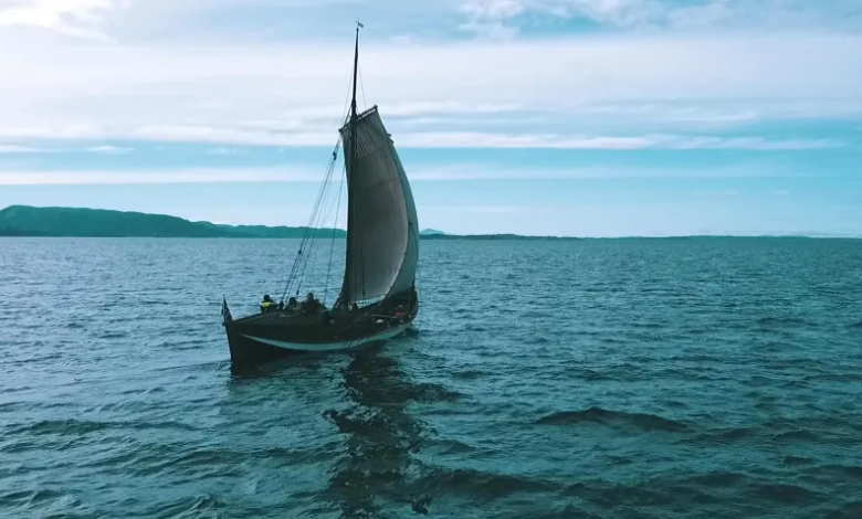 Perahu layar kecil membuatnya melintasi ombak pirus menuju cakrawala, biru muda dengan awan putih tipis