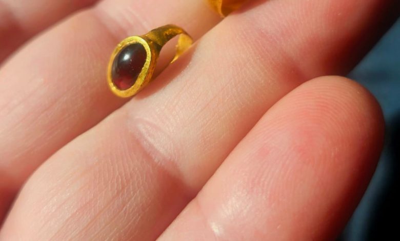 Seseorang memegang dua cincin emas batu permata yang ditemukan di lokasi pemakaman.