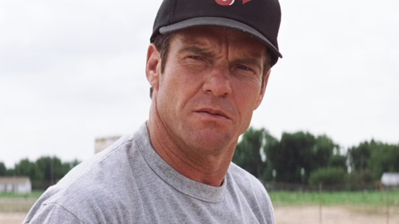 Close-up dari Dennis Quaid ketika Jimmy Morris berdiri di lapangan baseball, menyipit dengan intens saat mengenakan topi baseball dalam adegan dari pemula