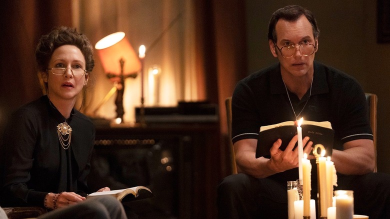 Vera Farmiga sebagai Lorraine Warren dan Patrick Wilson sebagai Ed Warren memegang Alkitab dan duduk di depan lilin di Conjuring 3
