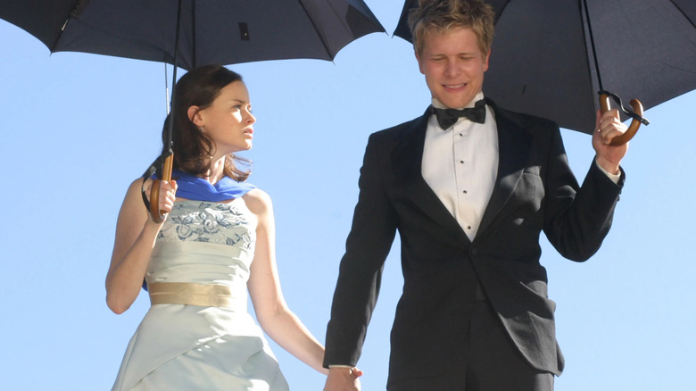 Rory dan Logan dalam pakaian formal memegang payung dan berpegangan tangan di Gilmore Girls