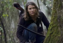 Lauren Cohan sebagai Maggie Greene berlutut di tepi pohon dengan busur dan panahnya di jalan mati