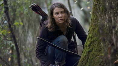 Lauren Cohan sebagai Maggie Greene berlutut di tepi pohon dengan busur dan panahnya di jalan mati