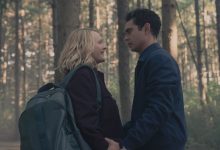 Juni (Elisabeth Moss) dan Nick (Max Minghella) berdiri dekat di hutan, berpegangan tangan saat June tersenyum hangat dan Nick menatapnya dengan intens dalam kisah pelayan