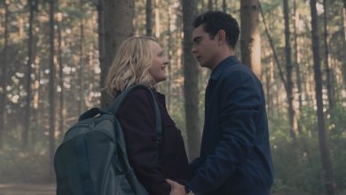 Juni (Elisabeth Moss) dan Nick (Max Minghella) berdiri dekat di hutan, berpegangan tangan saat June tersenyum hangat dan Nick menatapnya dengan intens dalam kisah pelayan