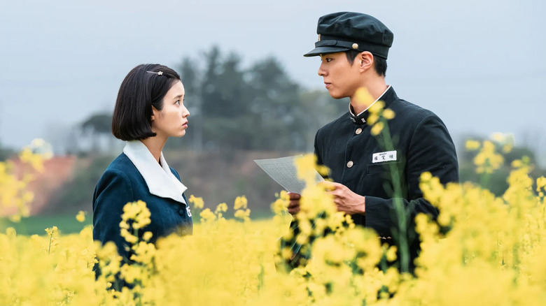 Oh ae-sun (IU) dan Yang Gwan-Sik (Park Bo-Gum) saling memandang di ladang bunga saat mengenakan seragam sekolah saat hidup memberi Anda jeruk keprok