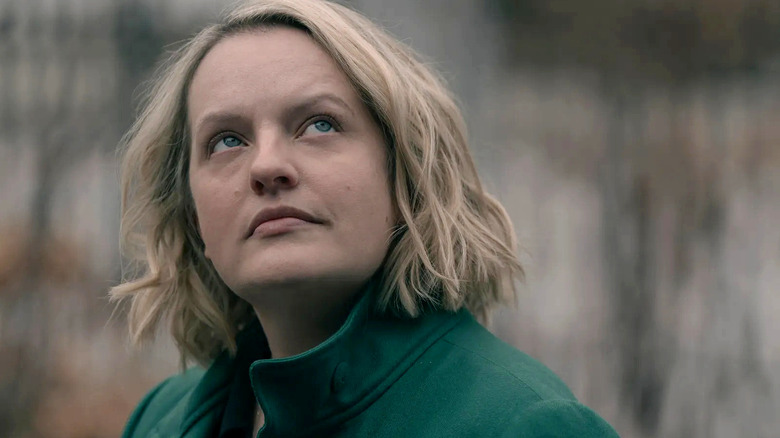 Juni (Elisabeth Moss) terlihat kontemplatif ke arah langit, mengenakan mantel hijau zamrud dalam kisah pelayan