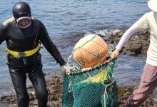 Dua wanita, satu di peralatan menyelam, mengangkut sekantong makanan laut di pantai
