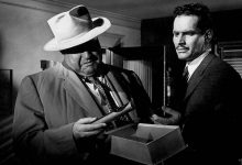 Orson Welles sebagai Hank Quinlan memeriksa bukti yang ditanam sebagai Charlton Heston sebagai Miguel Vargas terlihat berhubungan dengan kejahatan