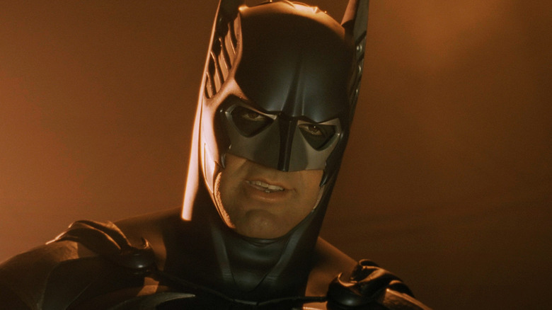 George Clooney sebagai Batman melihat ke bawah saat ia berdiri di depan latar belakang oranye di Batman & Robin