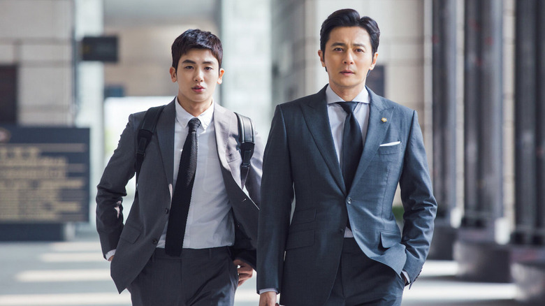 Go Yeon-Woo (Park Hyung-Sik) berjalan di belakang Choi Kang-Seok (Jang Dong-Gun) di lobi di Suits