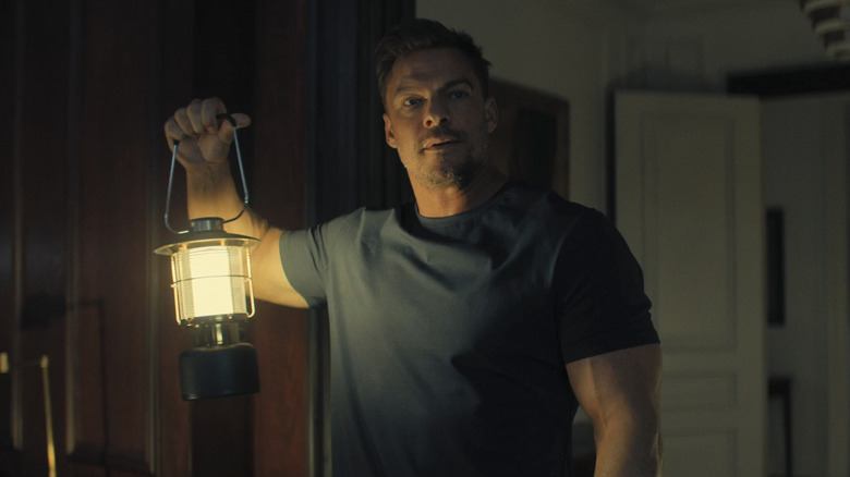 Alan Ritchson sebagai Jack Reacher memegang lentera di Reacher Season 3