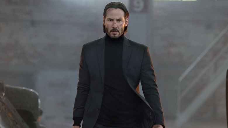 Keanu Reeves sebagai John Wick berjalan dengan mobil yang terbakar di gudang di John Wick