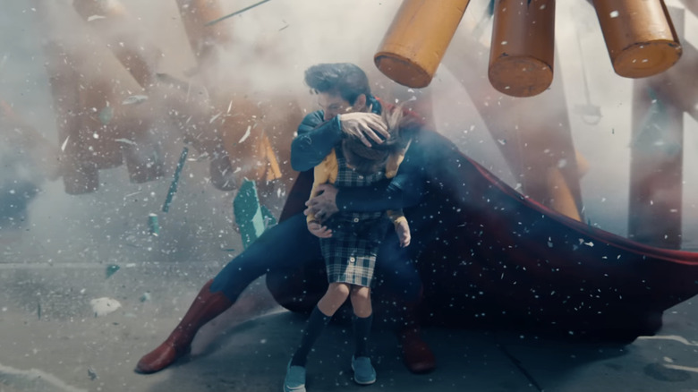 Superman melindungi seorang gadis kecil dari ledakan, melindunginya dengan tubuh dan jubahnya, di Superman